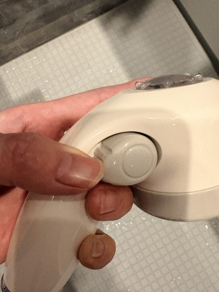 赤ちゃん用シャワーヘッドの手元ボタンでス水圧を切り替えている様子